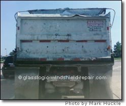 truck with damaged tarp and gravel falling out on the road